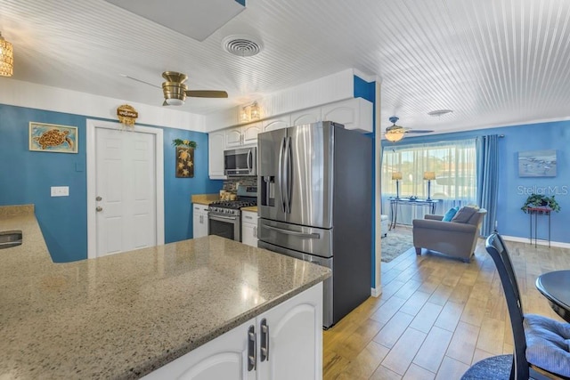 kitchen with appliances with stainless steel finishes, white cabinetry, kitchen peninsula, ceiling fan, and light stone counters