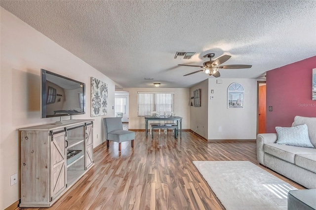 living room featuring ceiling fan, light hardwood / wood-style floors, and a textured ceiling