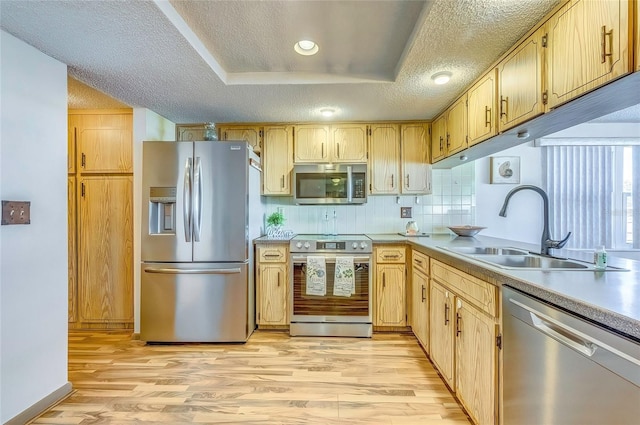 kitchen with sink, a textured ceiling, appliances with stainless steel finishes, a tray ceiling, and light hardwood / wood-style floors