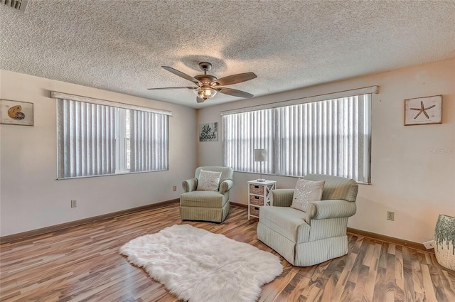 sitting room with ceiling fan, light wood-type flooring, and a textured ceiling