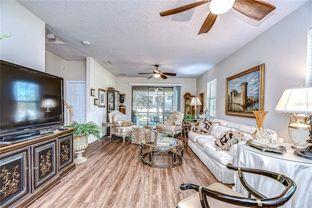 living room featuring ceiling fan, light hardwood / wood-style flooring, and a textured ceiling