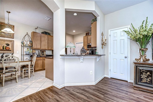 kitchen featuring kitchen peninsula, light wood-type flooring, decorative light fixtures, and a breakfast bar area