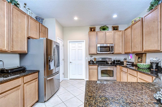 kitchen featuring dark stone counters, light tile patterned floors, a textured ceiling, light brown cabinetry, and stainless steel appliances