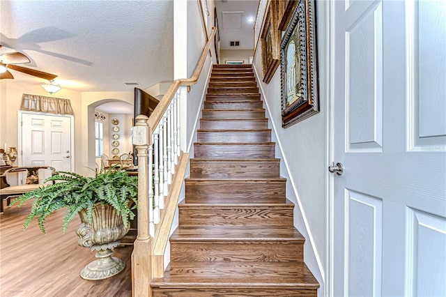 stairs with hardwood / wood-style flooring, ceiling fan, and a textured ceiling