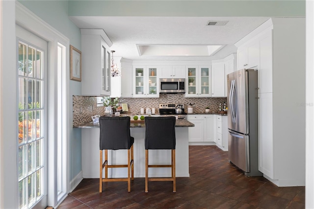 kitchen with a kitchen bar, tasteful backsplash, white cabinets, and appliances with stainless steel finishes