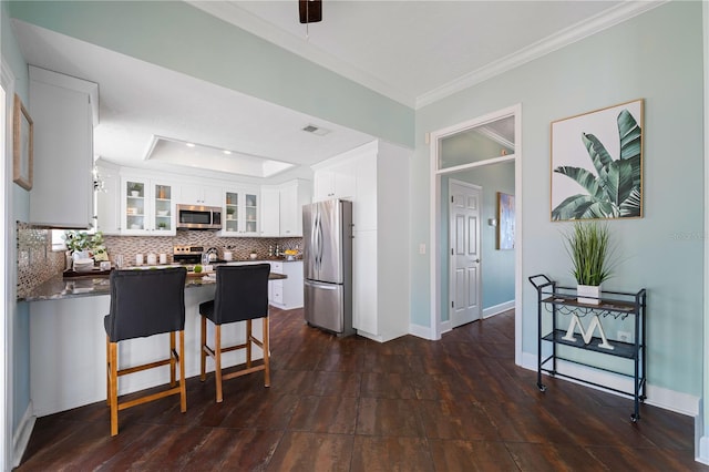 kitchen featuring white cabinets, a kitchen breakfast bar, decorative backsplash, ornamental molding, and appliances with stainless steel finishes