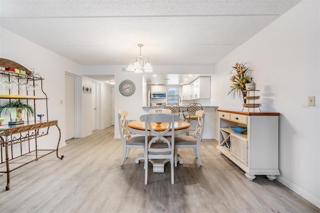 dining room featuring light wood-type flooring, a textured ceiling, and an inviting chandelier