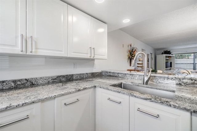 kitchen featuring white cabinetry, sink, and light stone counters