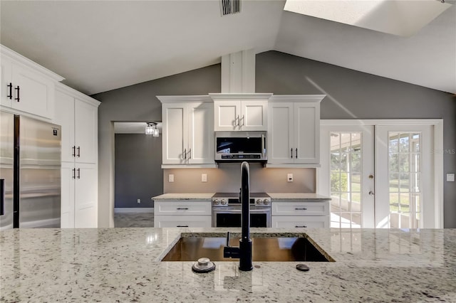 kitchen featuring french doors, white cabinets, vaulted ceiling, light stone countertops, and appliances with stainless steel finishes