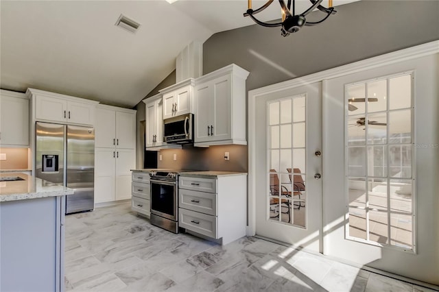 kitchen featuring white cabinetry, light stone counters, vaulted ceiling, ceiling fan with notable chandelier, and appliances with stainless steel finishes