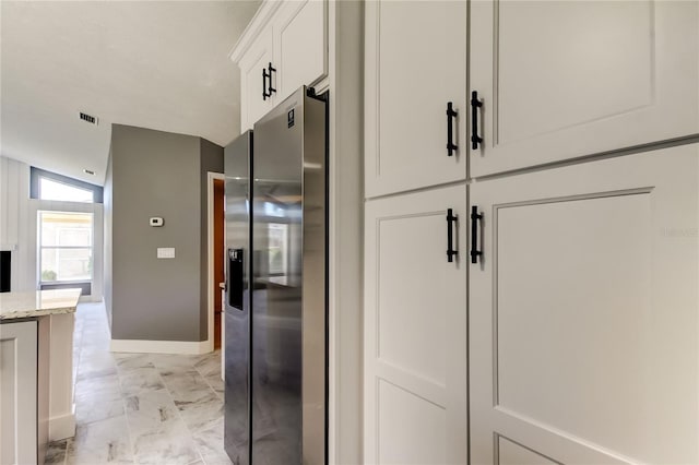 kitchen featuring stainless steel fridge, white cabinetry, light stone counters, and lofted ceiling