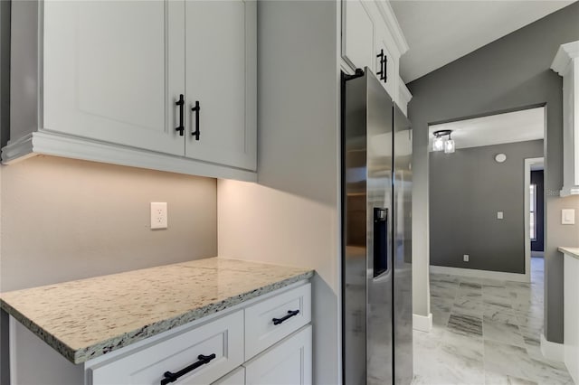 kitchen featuring light stone countertops, stainless steel fridge, and white cabinetry