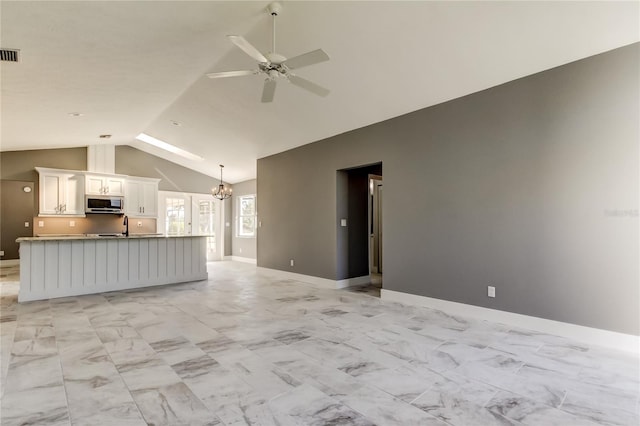 unfurnished living room featuring ceiling fan with notable chandelier, sink, and vaulted ceiling