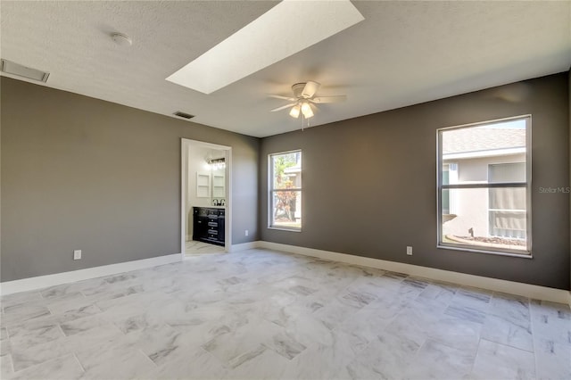 spare room featuring a skylight, ceiling fan, and a textured ceiling