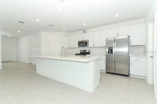 kitchen with stainless steel appliances, sink, white cabinets, an island with sink, and light tile patterned flooring