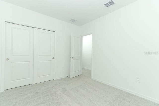 unfurnished bedroom with light colored carpet and a closet