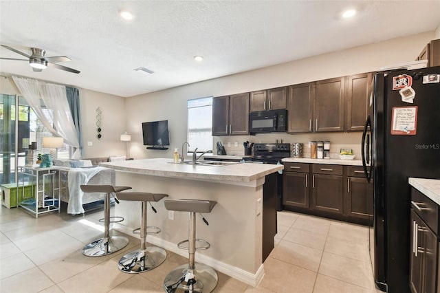 kitchen featuring a kitchen breakfast bar, dark brown cabinetry, a kitchen island with sink, sink, and black appliances