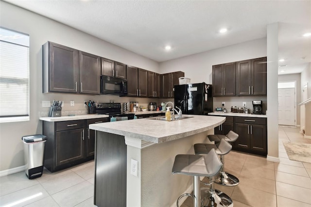 kitchen featuring sink, a kitchen island with sink, a breakfast bar, black appliances, and dark brown cabinets