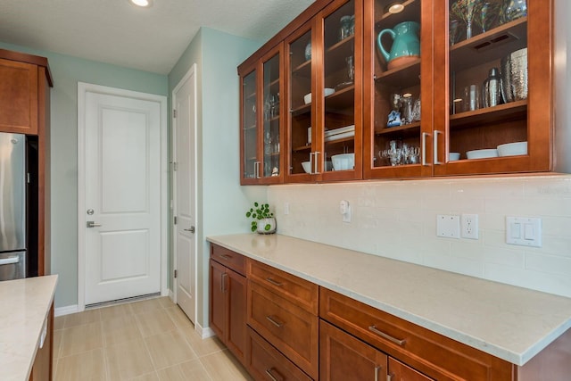 kitchen with light stone counters, backsplash, and stainless steel refrigerator