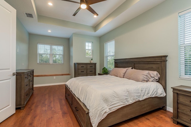 bedroom with dark wood-type flooring, ceiling fan, and a raised ceiling