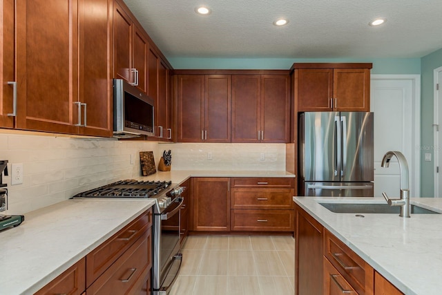 kitchen with sink, appliances with stainless steel finishes, light stone counters, tasteful backsplash, and a textured ceiling