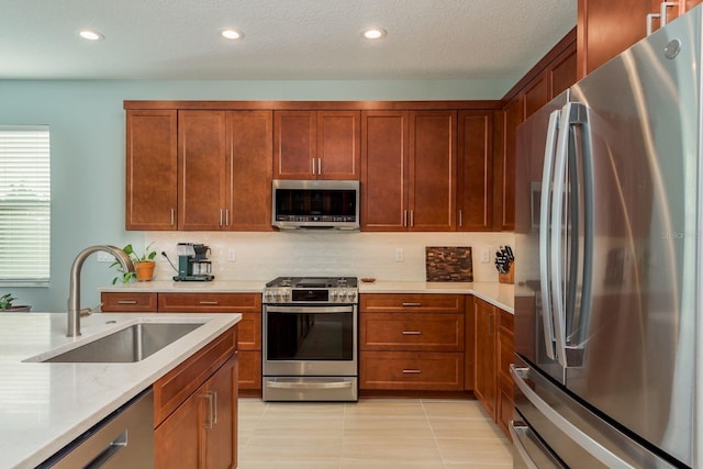 kitchen with light tile patterned flooring, sink, light stone counters, a textured ceiling, and stainless steel appliances