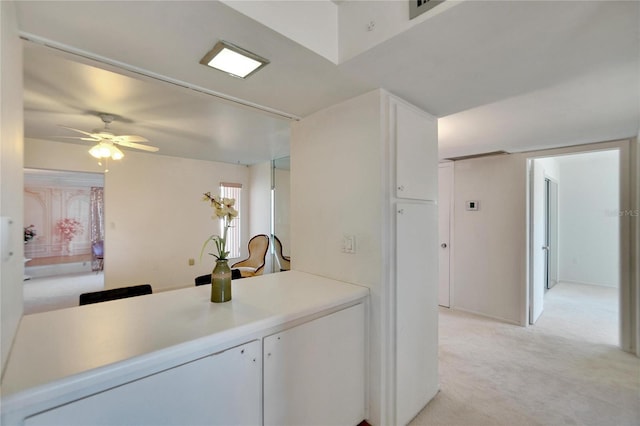 kitchen featuring white cabinetry, ceiling fan, and light colored carpet