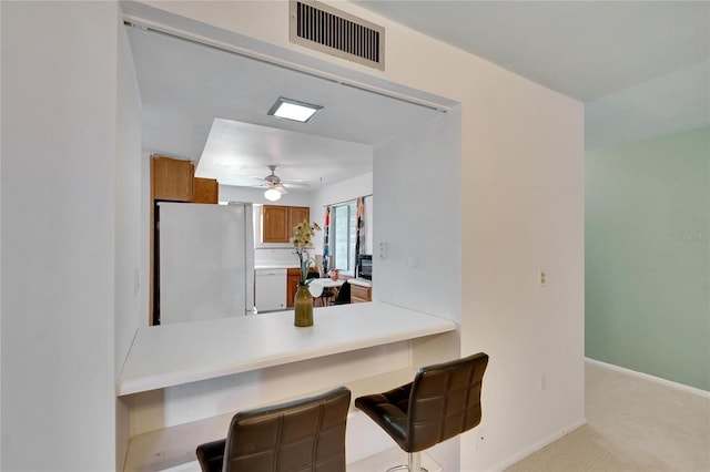 kitchen featuring light carpet, a kitchen breakfast bar, white refrigerator, ceiling fan, and kitchen peninsula