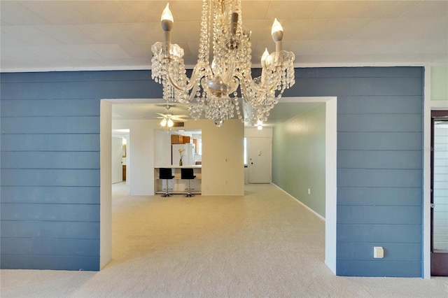 unfurnished dining area with carpet, ceiling fan with notable chandelier, and ornamental molding