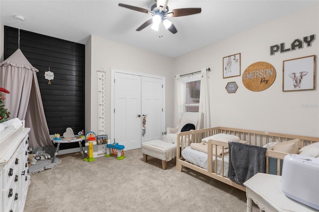 bedroom with a closet, light carpet, ceiling fan, and a crib