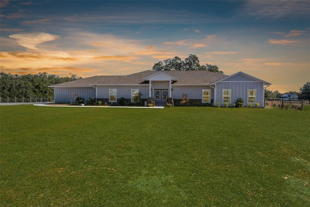 ranch-style home featuring french doors, board and batten siding, fence, and a lawn