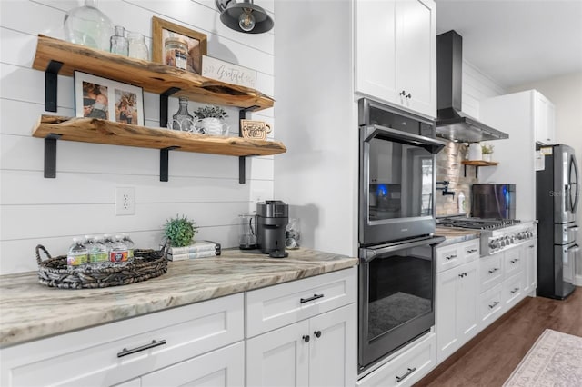 kitchen featuring white cabinets, dark wood-type flooring, stainless steel appliances, wall chimney range hood, and open shelves