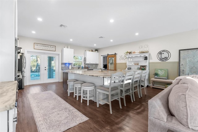 kitchen with a barn door, a wainscoted wall, visible vents, white cabinetry, and french doors