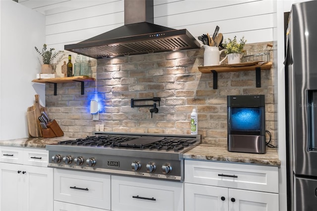 kitchen with appliances with stainless steel finishes, white cabinets, wall chimney exhaust hood, and tasteful backsplash