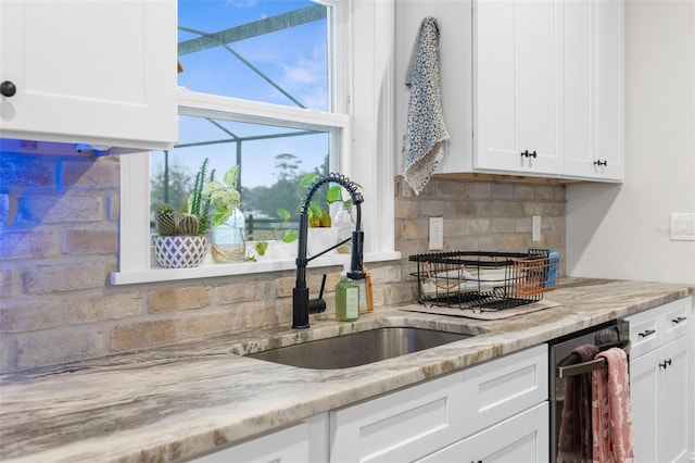 kitchen featuring light stone counters, a sink, white cabinetry, and decorative backsplash