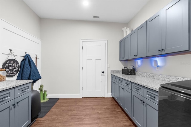 kitchen featuring light stone counters, wood finished floors, range, and baseboards