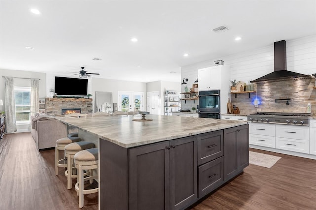 kitchen featuring dobule oven black, stainless steel gas cooktop, white cabinetry, visible vents, and wall chimney exhaust hood