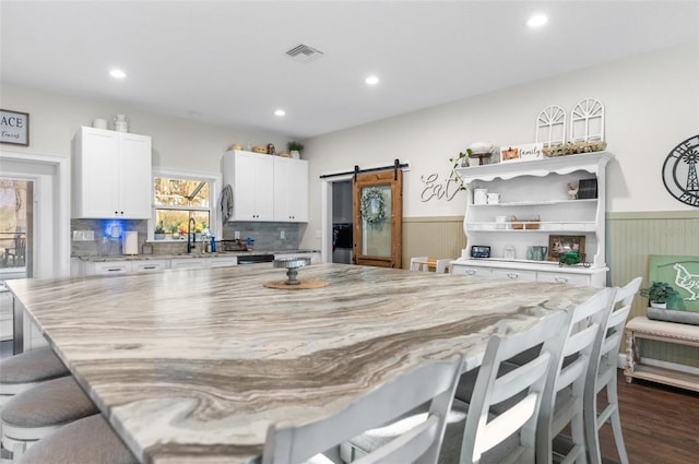 kitchen with a barn door, visible vents, white cabinets, wainscoting, and a kitchen bar