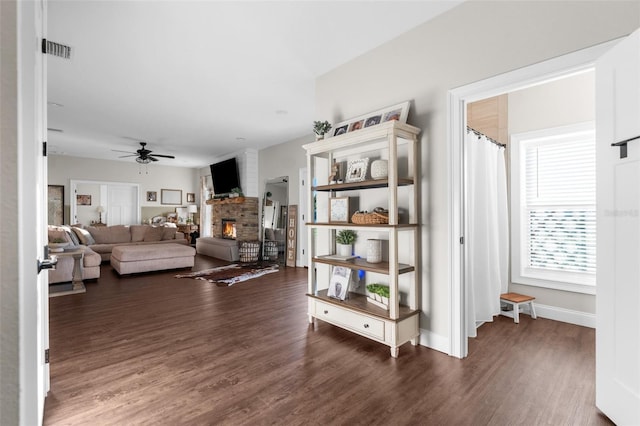 living room with a warm lit fireplace, a ceiling fan, visible vents, and wood finished floors