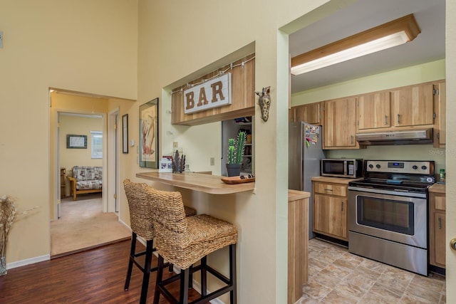 kitchen with kitchen peninsula, appliances with stainless steel finishes, light hardwood / wood-style flooring, and a kitchen breakfast bar