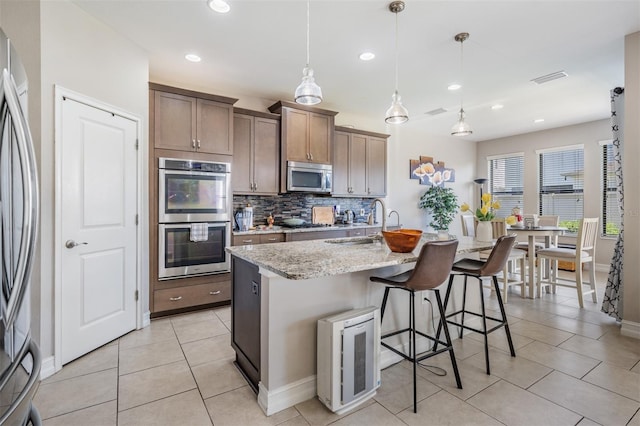 kitchen featuring light stone counters, hanging light fixtures, an island with sink, and stainless steel appliances