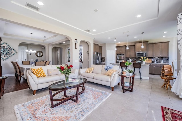 living room featuring a raised ceiling, light hardwood / wood-style floors, and an inviting chandelier