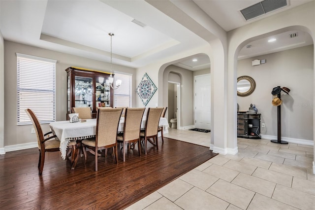 dining room featuring a raised ceiling, light hardwood / wood-style flooring, a chandelier, and plenty of natural light