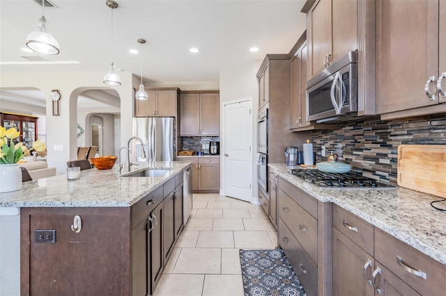 kitchen featuring backsplash, sink, light stone countertops, an island with sink, and stainless steel appliances