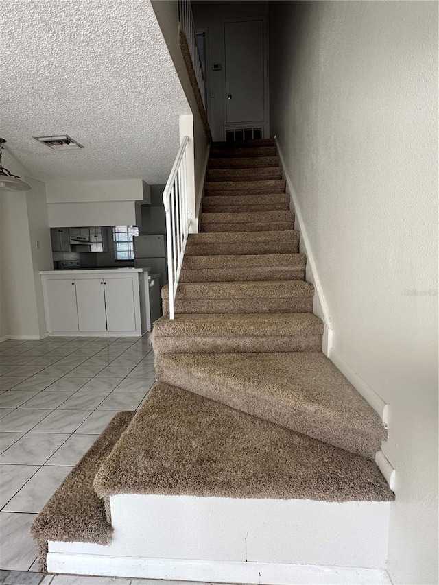 stairs featuring tile patterned flooring and a textured ceiling