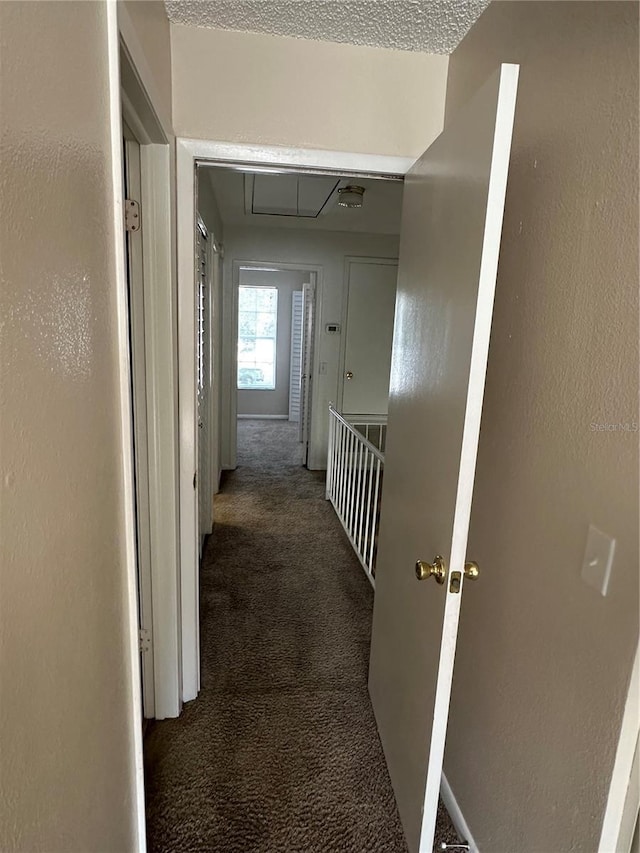 corridor with dark carpet and a textured ceiling