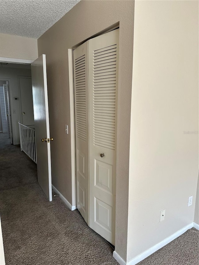 hallway with dark colored carpet and a textured ceiling