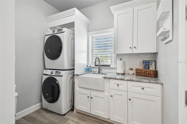 laundry room with light hardwood / wood-style floors, cabinets, stacked washing maching and dryer, and sink