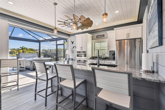 kitchen featuring hanging light fixtures, light stone counters, appliances with stainless steel finishes, white cabinets, and light wood-type flooring