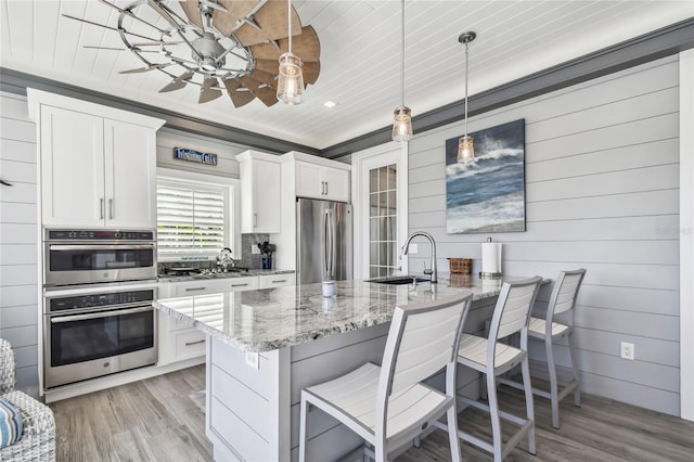 kitchen featuring light stone countertops, light hardwood / wood-style flooring, pendant lighting, white cabinets, and appliances with stainless steel finishes